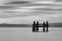 A mono shot of the old wartime pier posts between Lepe and Calshot. The picture was a long exposure, making the sea flat and mist-like, and the clouds like pastel patterns.