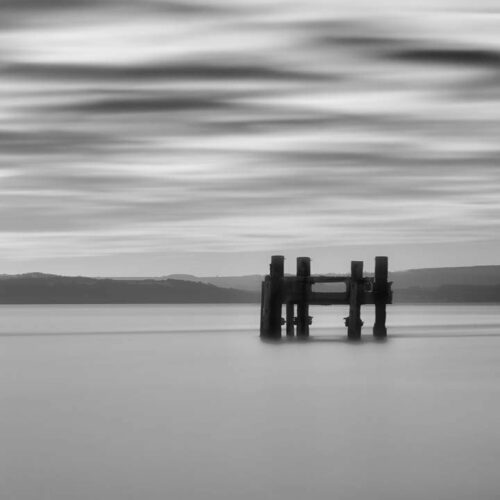 A mono shot of the old wartime pier posts between Lepe and Calshot. The picture was a long exposure, making the sea flat and mist-like, and the clouds like pastel patterns.